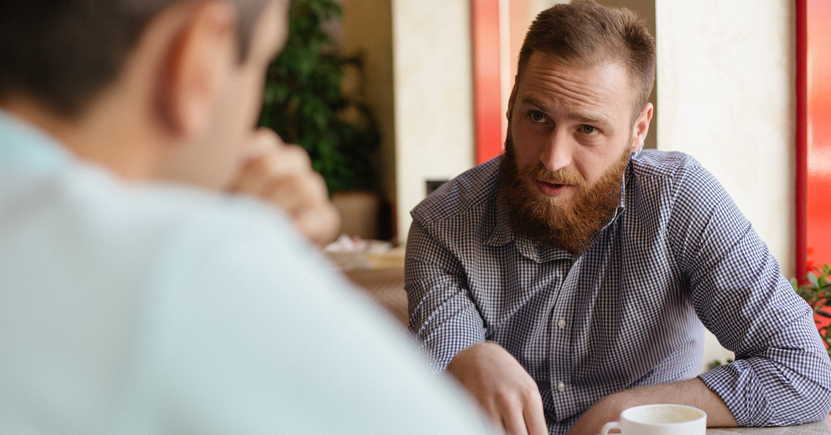 A man chatting with another, over a coffee