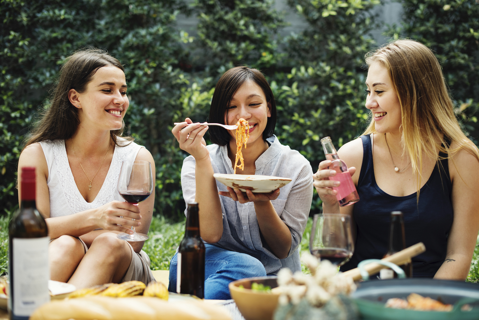 Three friends joyfully eating pasta together