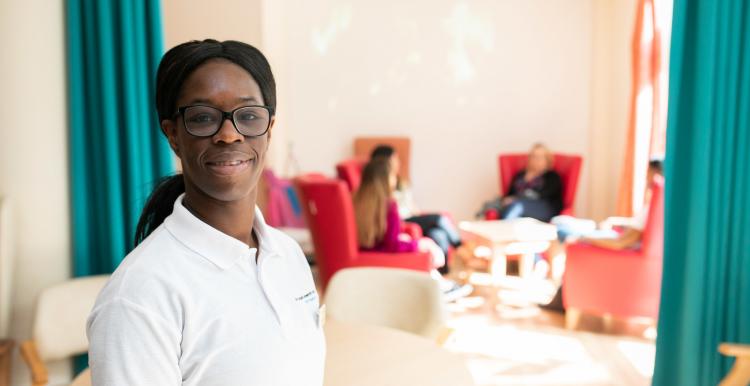 Health professional standing in a room with patients sitting in the background