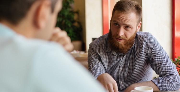 A man chatting with another, over a coffee