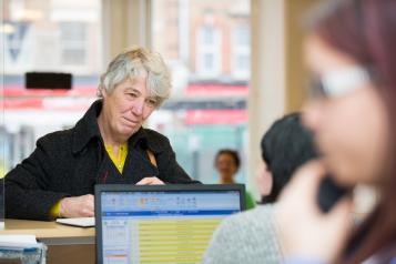 Older woman at a GP reception desk trying to book a GP appointment.