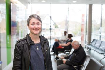 Woman standing within a waiting room. There are people sitting on the chairs and waiting. 