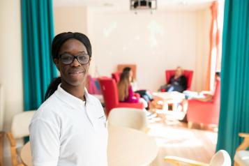 Health professional standing in a room with patients sitting in the background