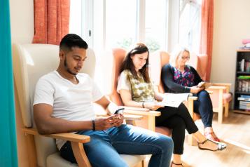 Three people sitting in an hospital waiting room, keeping themselves occupied with magazines and their smartphones