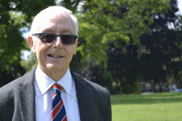 A picture of Alan smiling at the camera, standing in a park on a lovely sunny day.