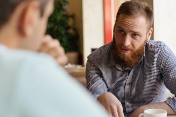 A man chatting with another, over a coffee