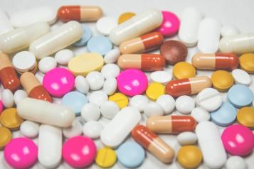 A variety of pills spread out on a white worktop. 