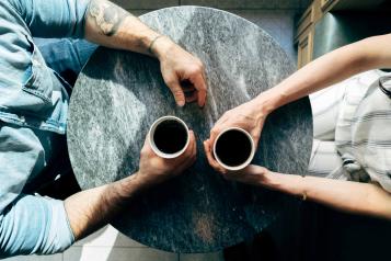 Two people sitting at a coffee table with there arms over the table. 