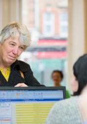 Older woman at a GP reception desk trying to book a GP appointment.