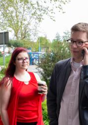 A man is on the phone and the woman next to him is looking at him and holding a hot drink. 