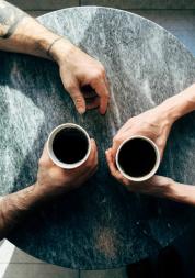 Two people sitting at a coffee table with there arms over the table. 